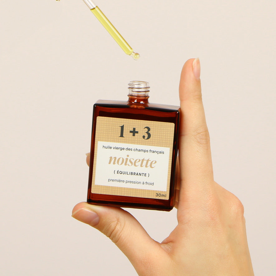 Mains tenant l’huile de noisette 1+3 – équilibrante et adoucissante, idéale pour les peaux mixtes à grasses